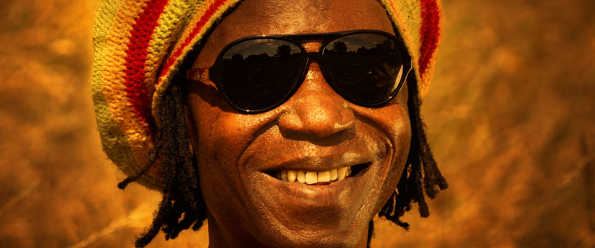 Hif Anga, lachend mit Sonnenbrille und Rastamütze